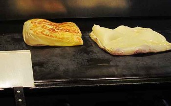 Egg roti and one with red onions inside puff and sizzle on the grill at Mamak restaurant.